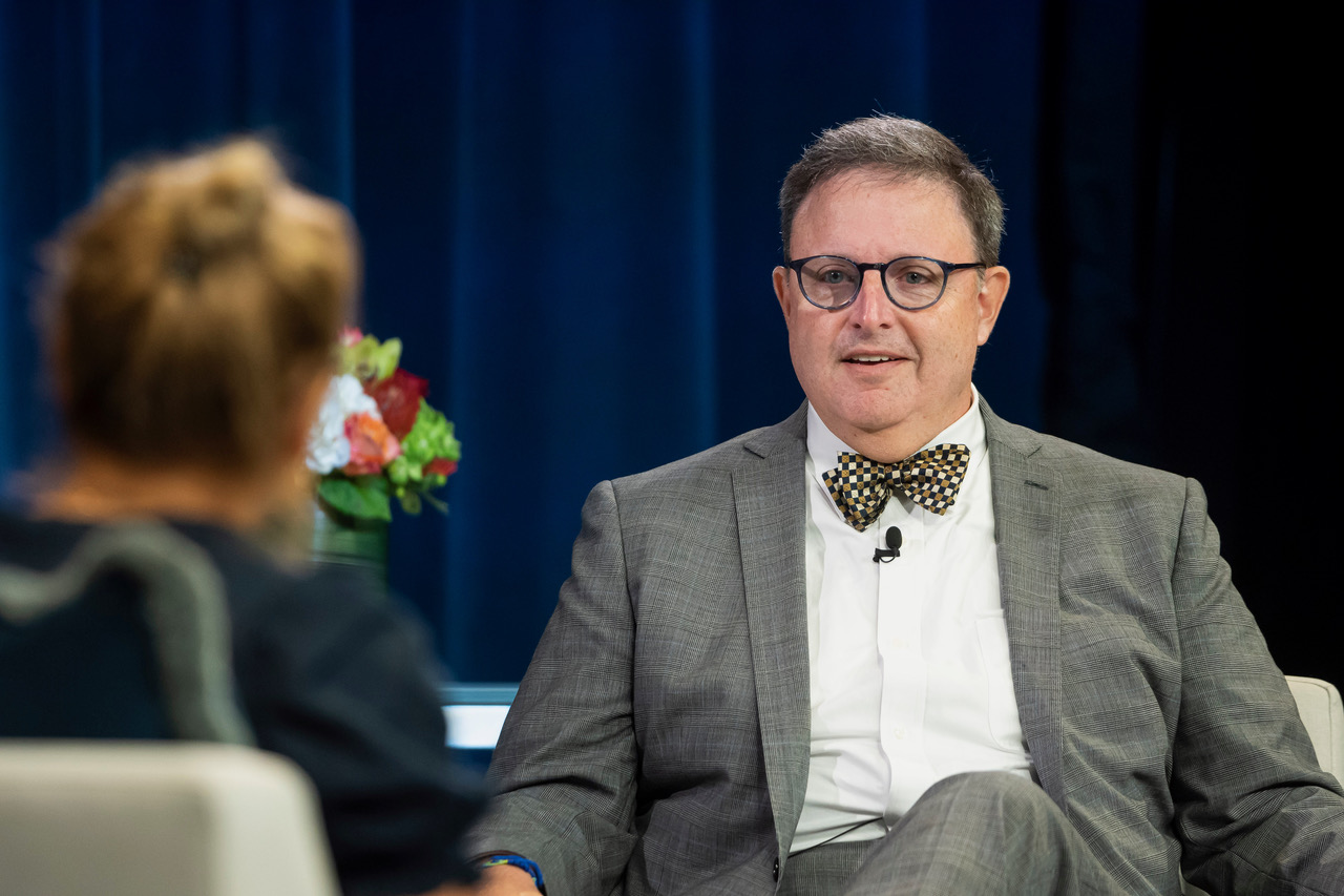 Jamie Lassner at a professional speaking engagement, wearing a gray suit and bowtie